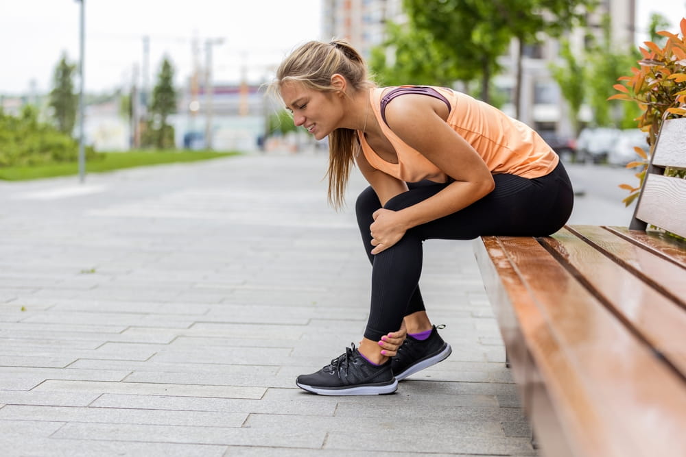 Running injury leg accident- sport woman runner hurting holding painful sprained ankle in pain.