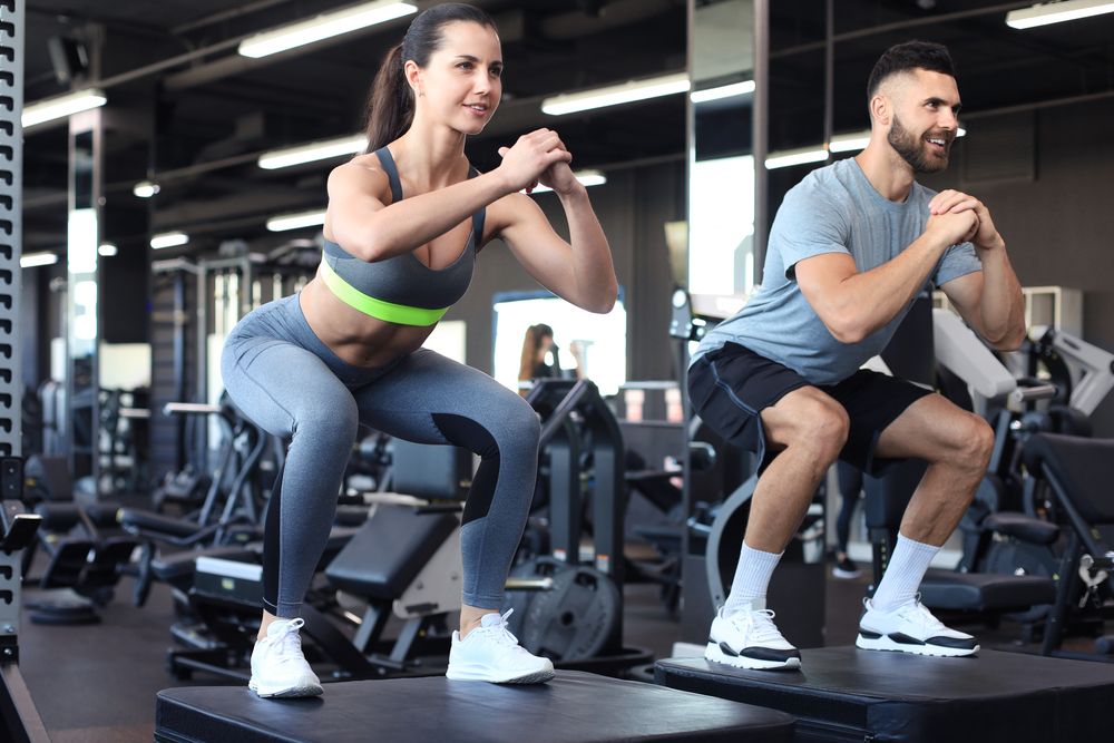 Fit couple doing jumping squats in crossfit gym