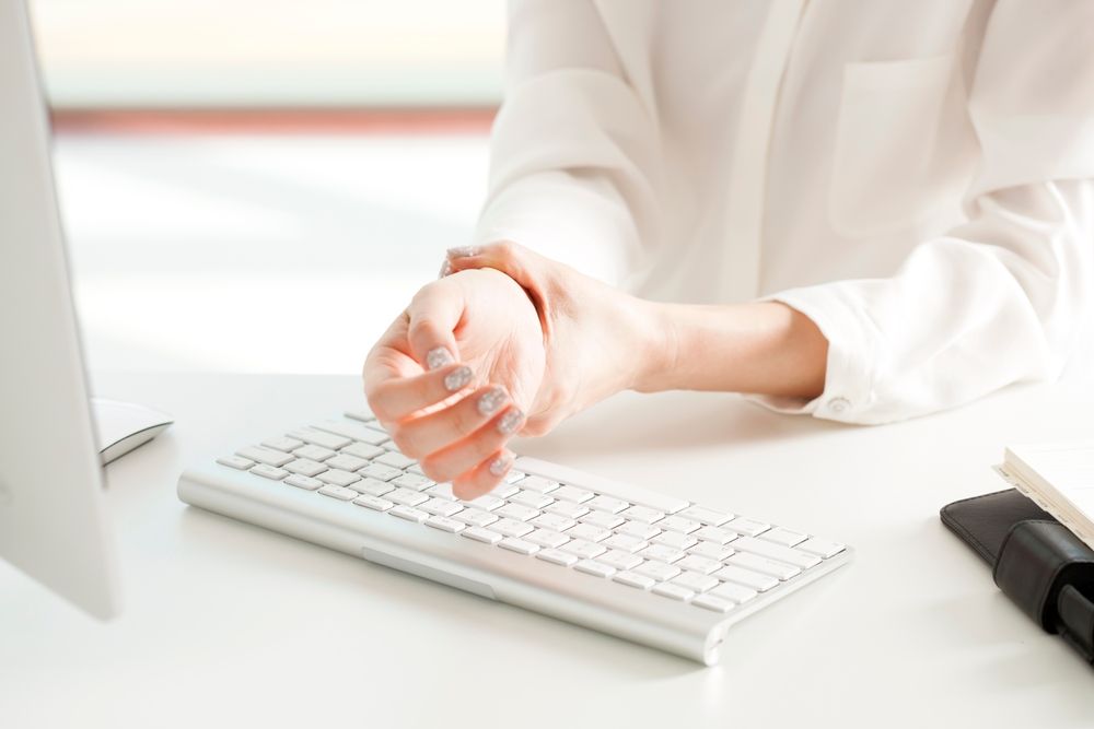 Wrist pain after long hours of typing at a computer desk in a bright and modern office setting during the day