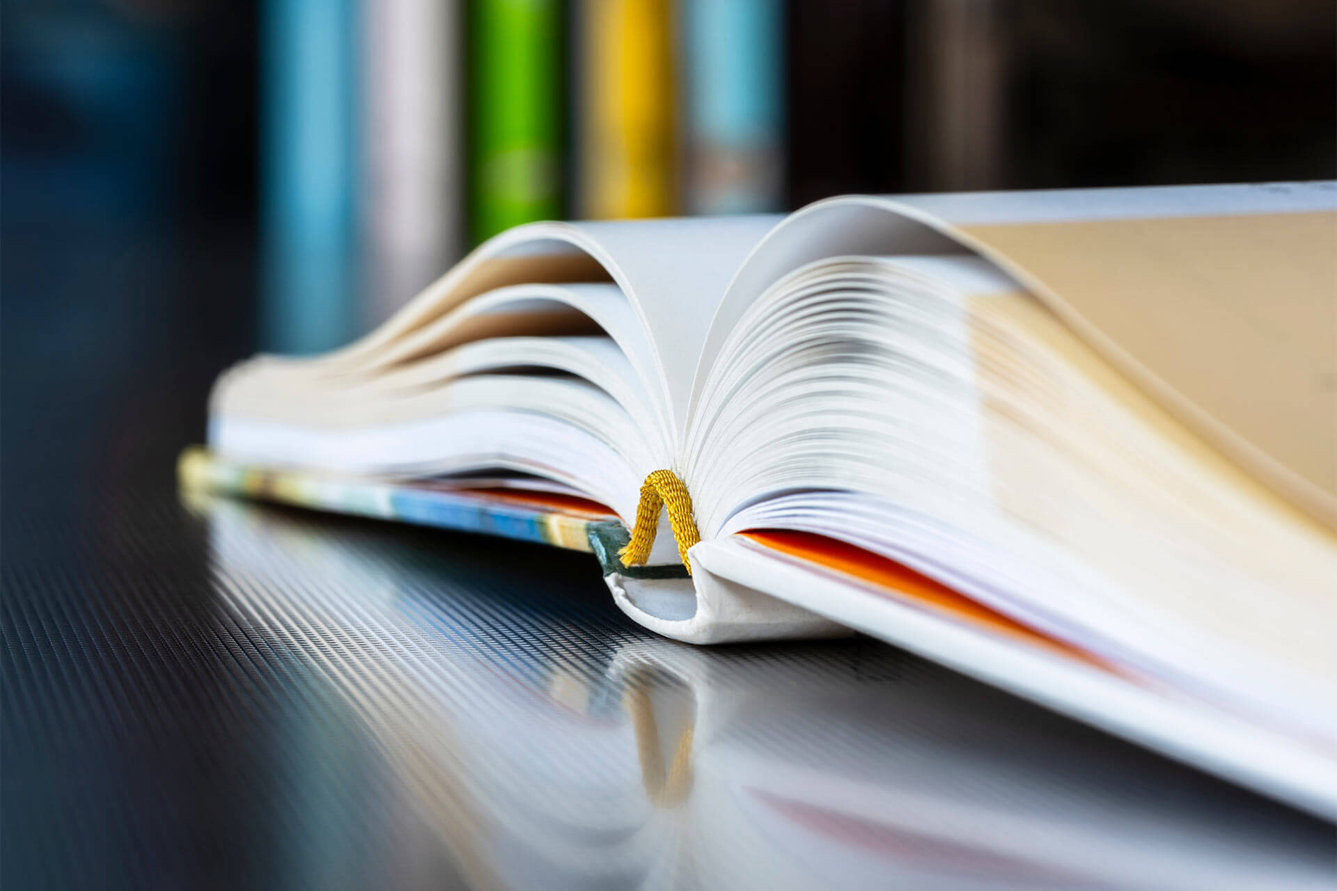 Close-up opened book with reflection on metal desk, library bookshelf in toned background
