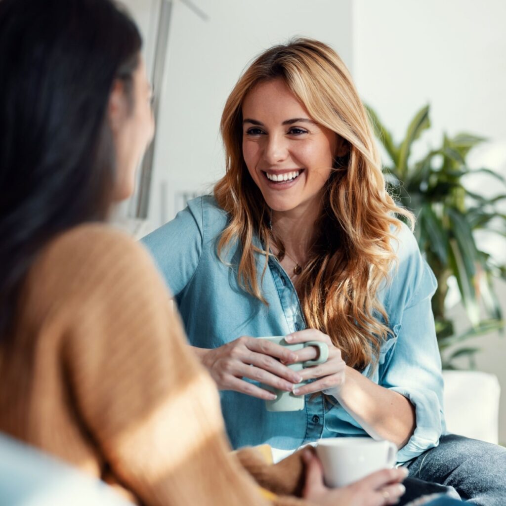 two smiling young women talking while drinking coffee