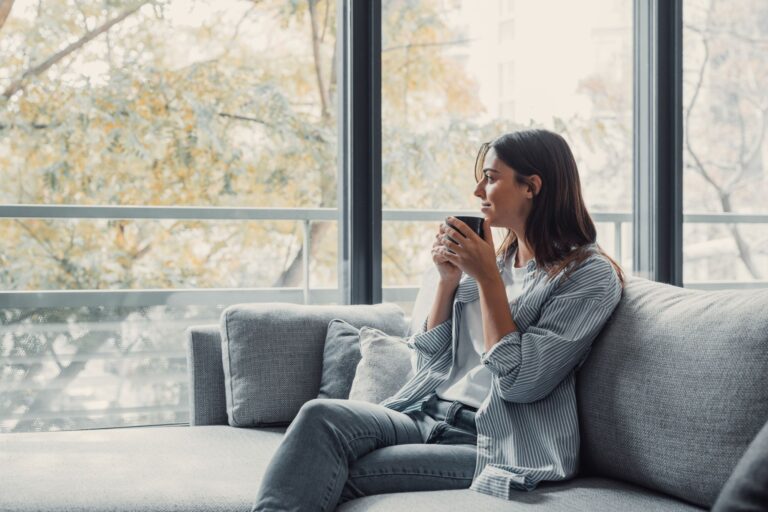 Cheerful dreamy girl holding mug of hot beverage