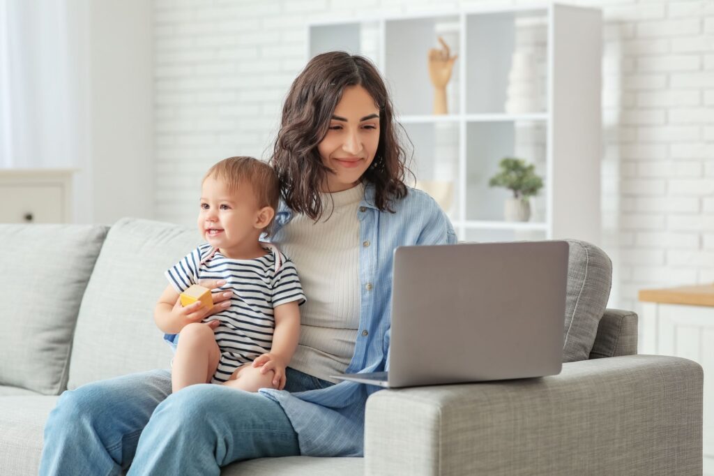 Cute baby and happy young mother working with laptop