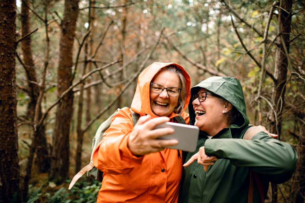 Senior women friends laughing together on forest hike in raincoats