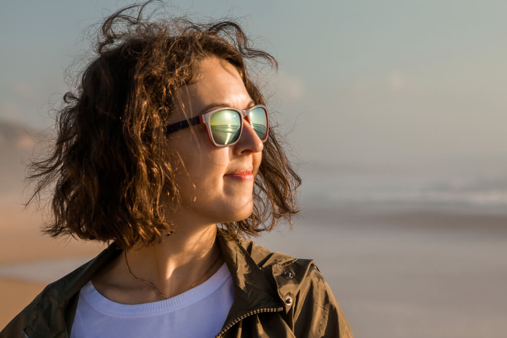 Portrait of young and stylish woman standing on the beach during sunset