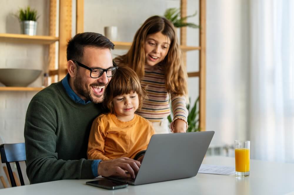 Happy family with kids having fun using laptop together, parent and children relaxing at home