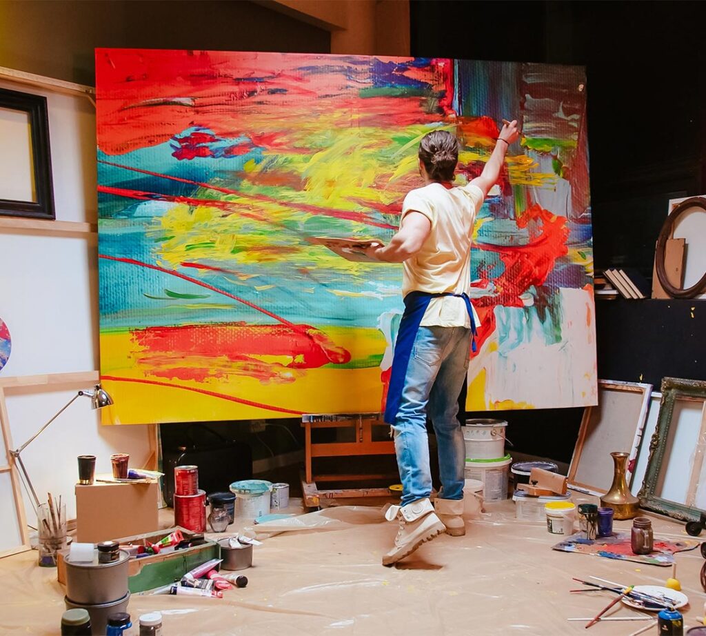 Back view of young Caucasian man painter emotionally drawing on big canvas
