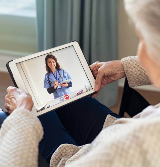 Back view of senior woman sitting in wheelchair making video call with her doctor