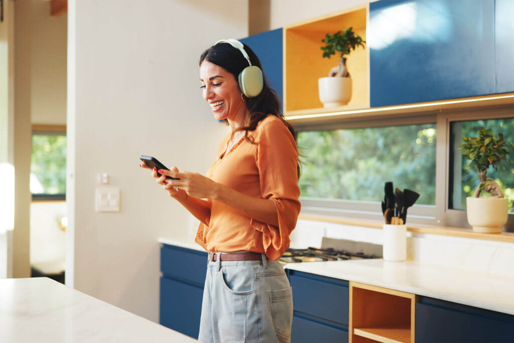 Phone, headphones and woman in kitchen in home listening to music