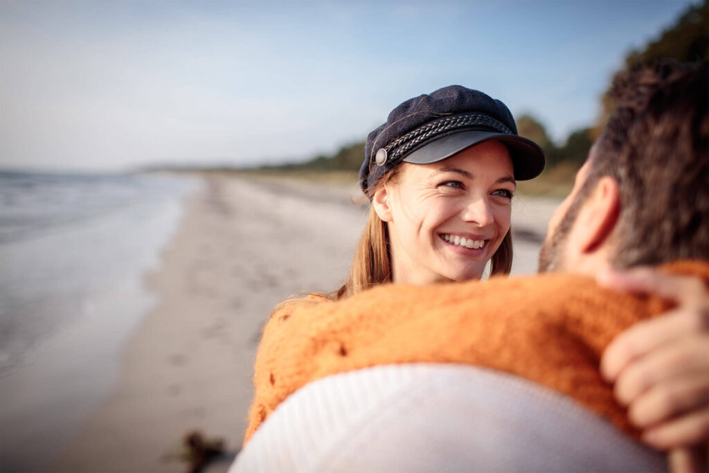 Happy young couple hugging and laughing together on the beach during a sunny autumn day