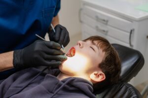 A dentist checks the teeth of a child who is sitting in an armchair
