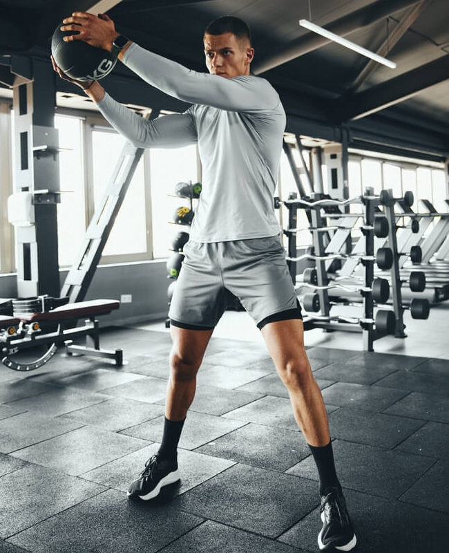 Vertical photo of a muscular man working out with a medicine ball in a gym setting