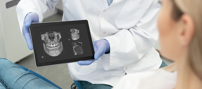 Dental consultation in clinic. Dentist showing teeth x-ray on digital tablet screen. 3D tomography technology.