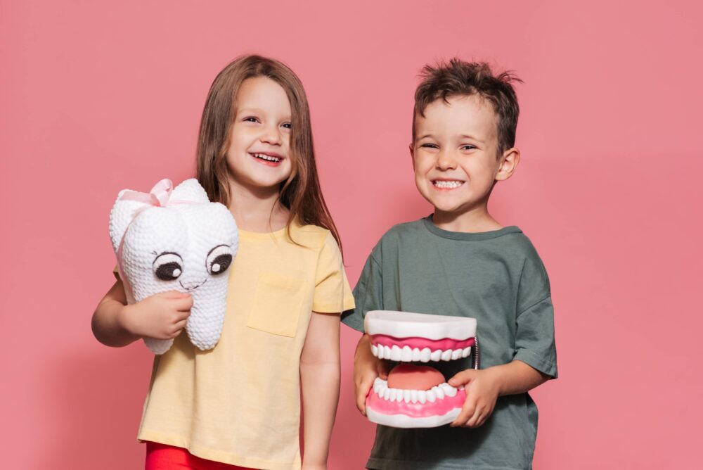 A smiling boy and a girl with healthy teeth hold a toy tooth in their hands on an isolated background.