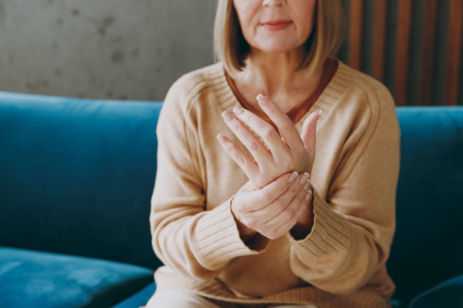 elderly woman 50s years old wearing casual clothes sits on blue sofa do self hand massage