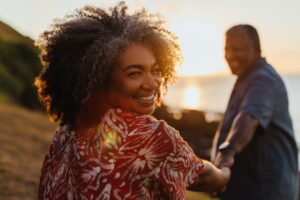 Senior woman embracing longevity and vitality while walking at sunset, holding her partner’s hand and smiling warmly.
