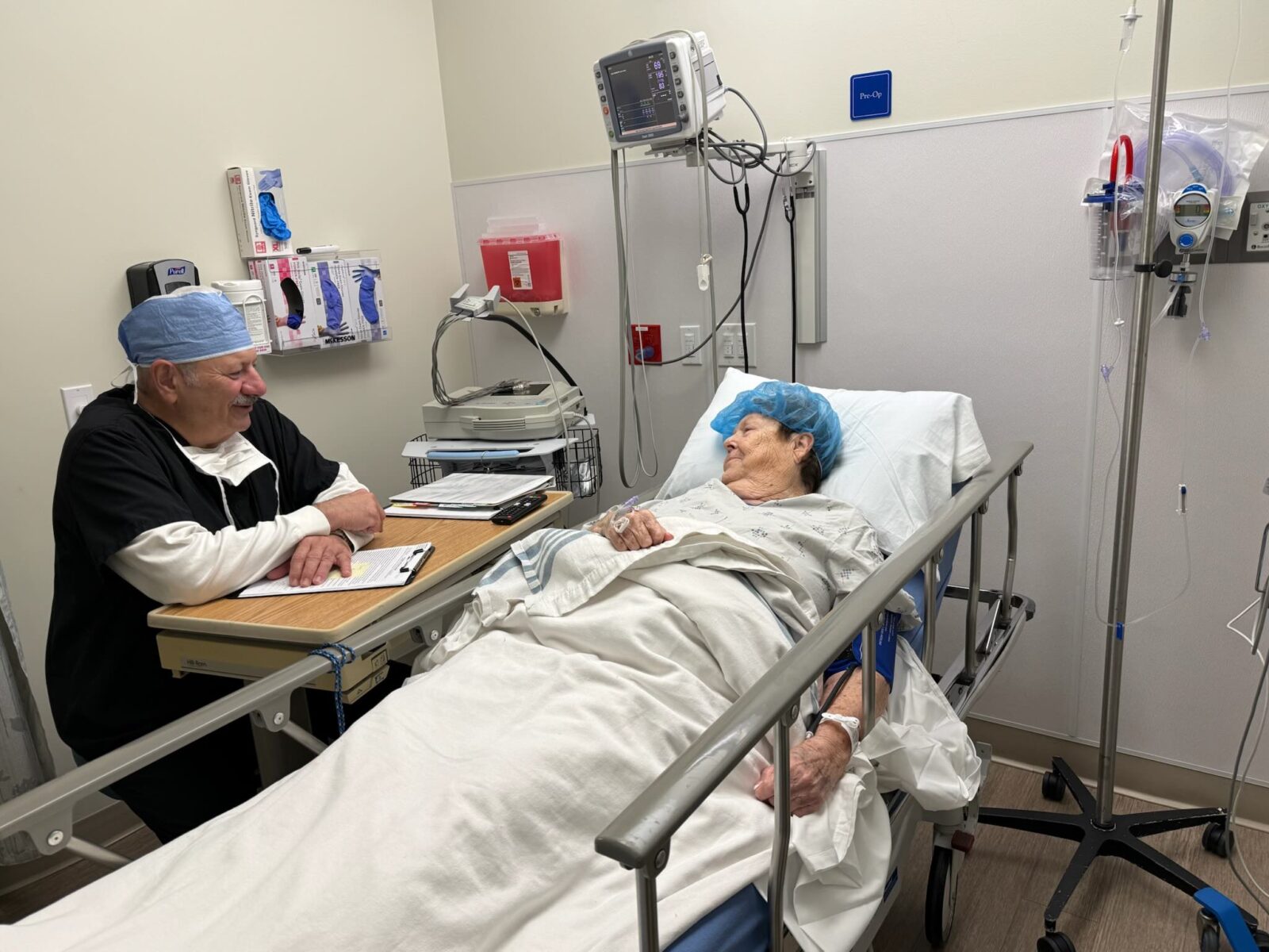 A medical professional in scrubs is seated nearby, likely reviewing charts or discussing the patient's care.