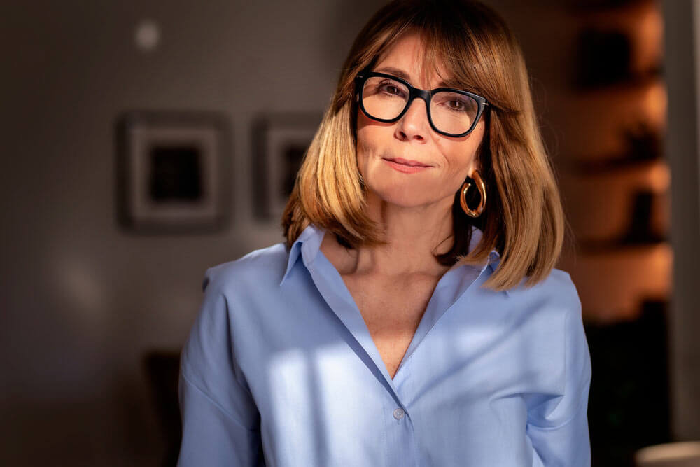 A confident middle-aged woman with shoulder-length blond hair and stylish glasses