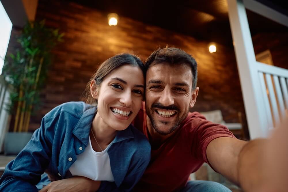 Happy new homeowners taking selfie on the porch and looking at camera.