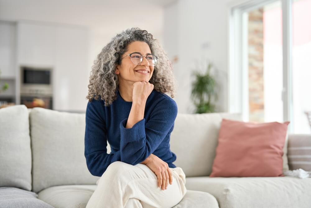 Happy relaxed 50 years old woman sitting on sofa at home looking away