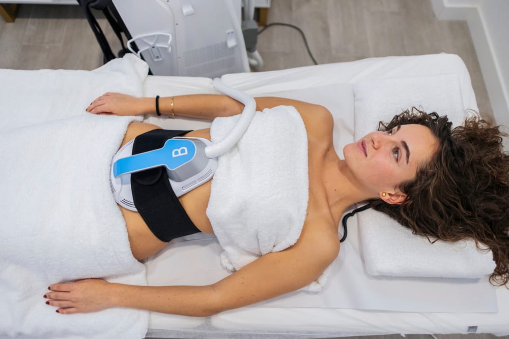 Woman lying on a bed receiving an aesthetic medicine treatment on her abdomen, targeting fat reduction and body contouring