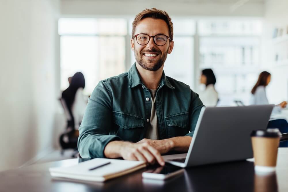 man sitting in an office with his colleagues in the background.