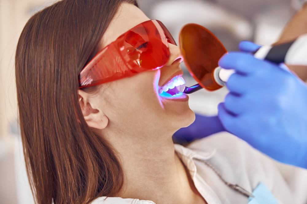 Professional male doctor uses ultraviolet lamp after making a filling on a tooth