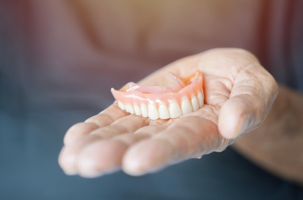 An elderly man holds a denture.