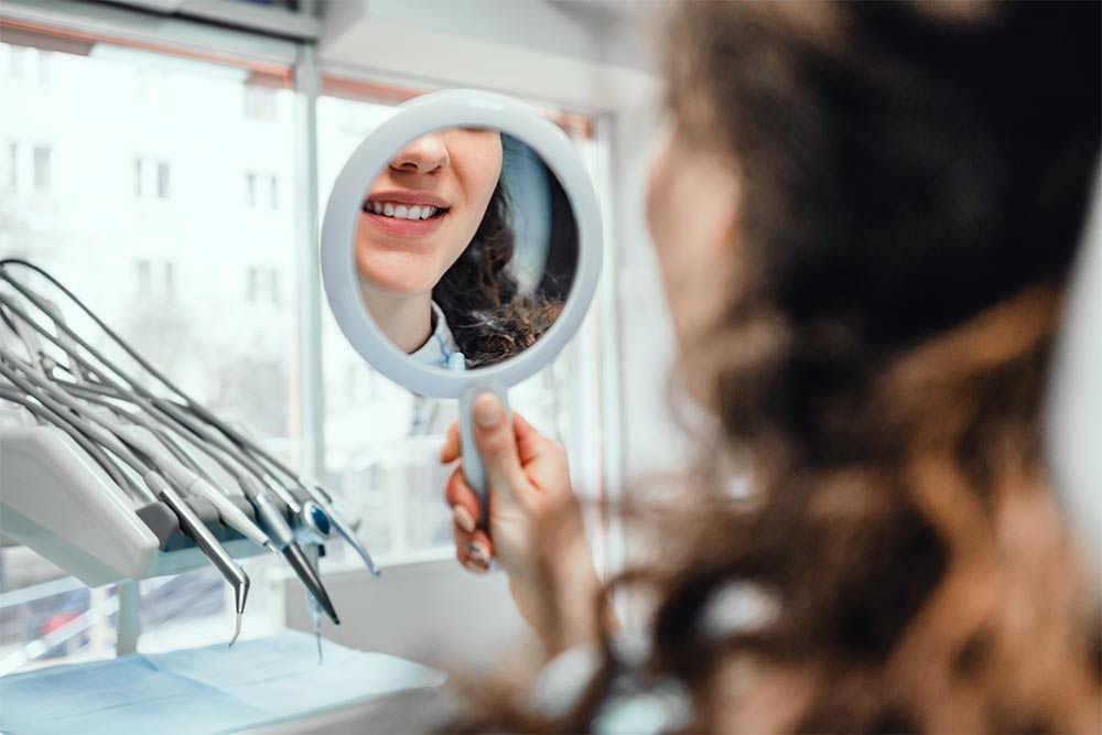 Beautiful girl sits in the dentist's chair and looks at herself in the mirror.