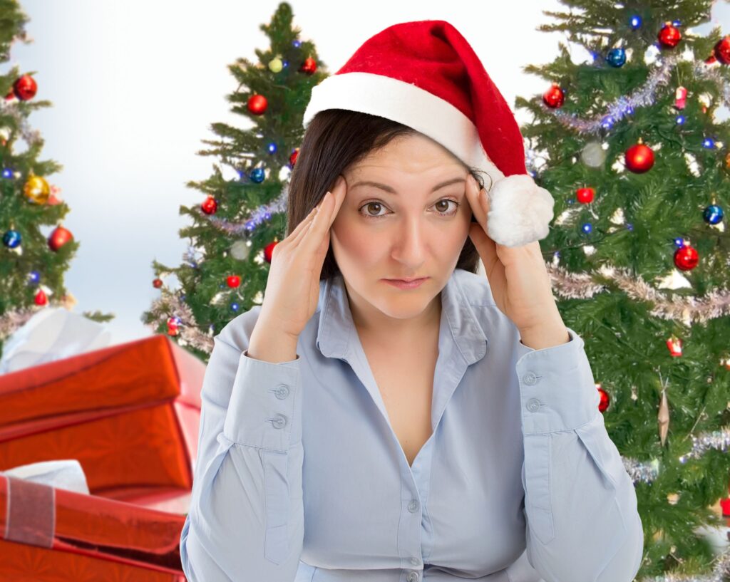 Stressed out looking woman wearing santa hat with Christmas tree in background