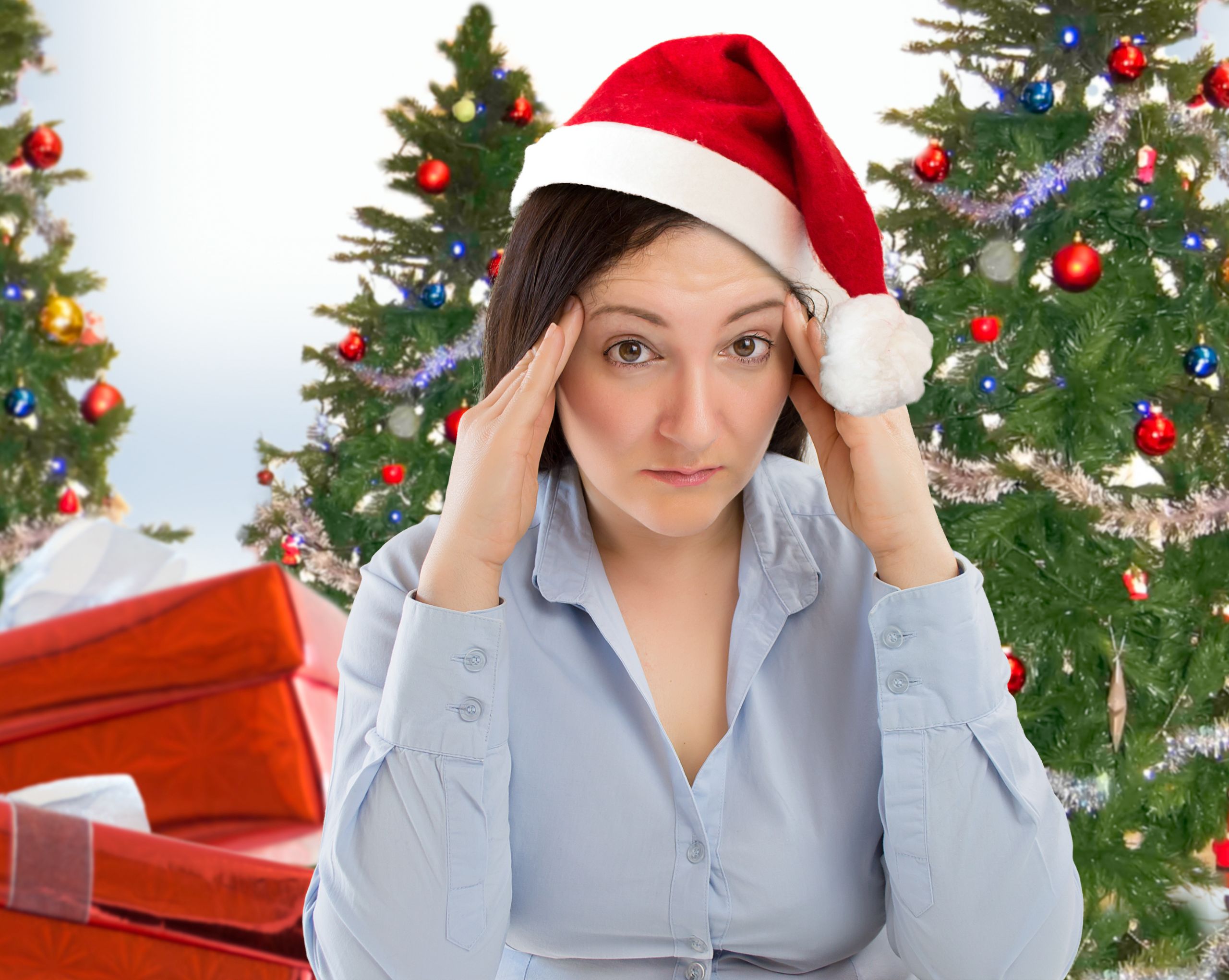 Stressed out looking woman wearing santa hat with Christmas tree in background