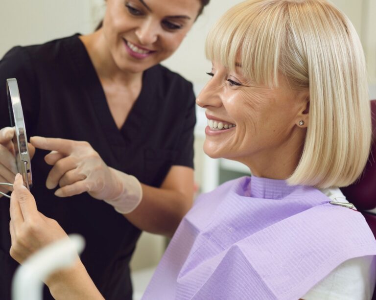 Female dental patient looking in mirror while dental assistant looks on