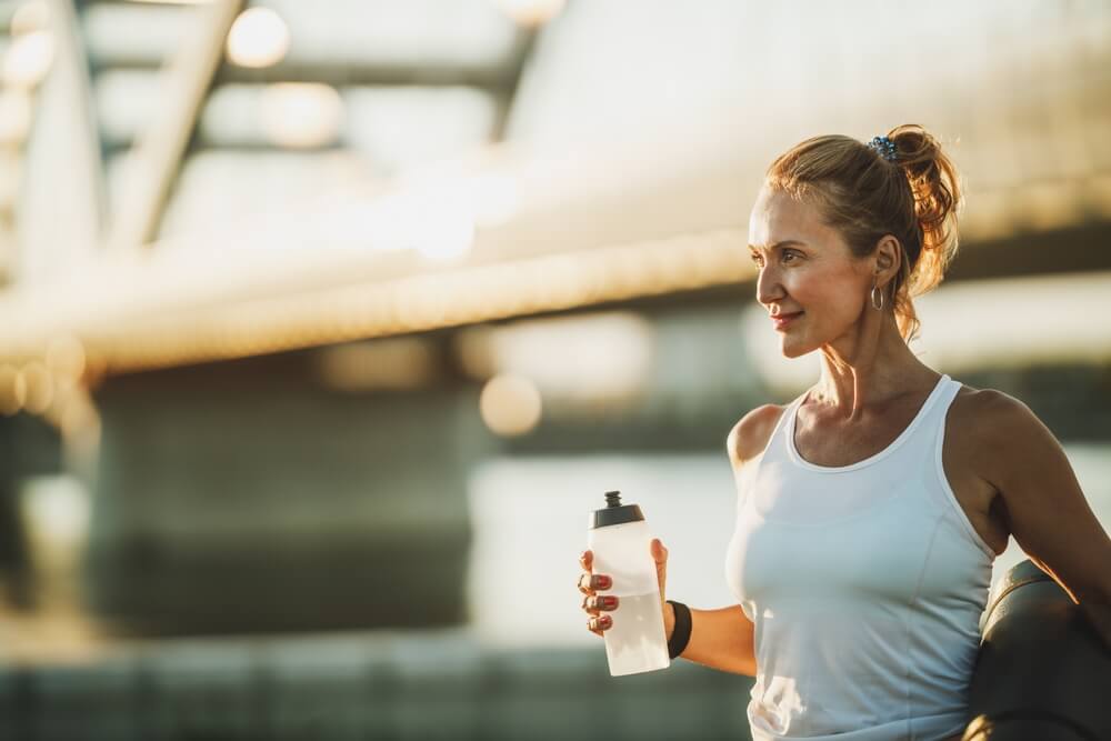 Middle age sportswoman holding water bottle before training