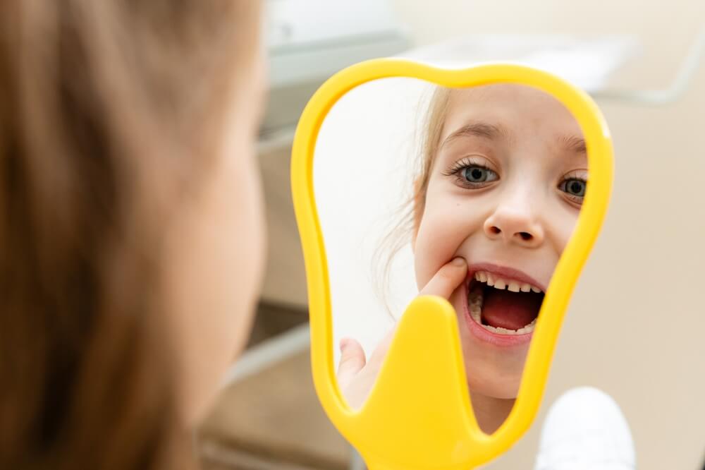 Lovely little girl looking in the mirror at her teeth after teeth surgery