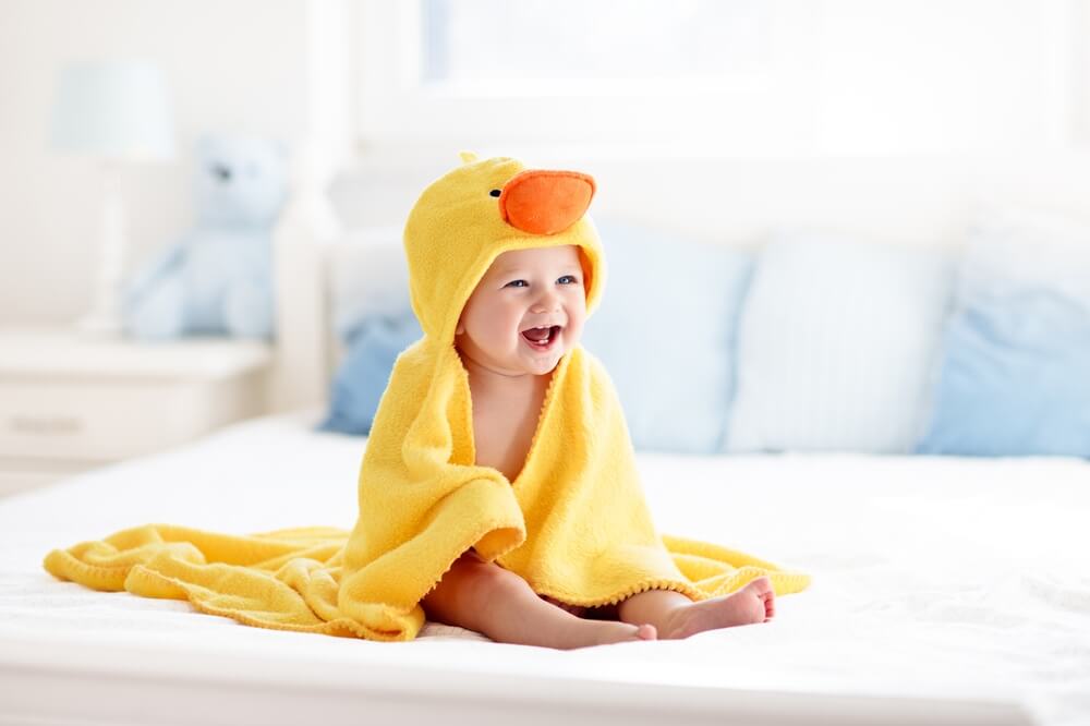 Happy laughing baby wearing yellow hooded duck towel