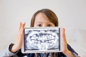 Young boy holding up a smart device that shows an x-ray of mouth