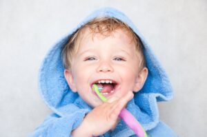 Young toddler in restroom smiling and brushing teeth looking at camera