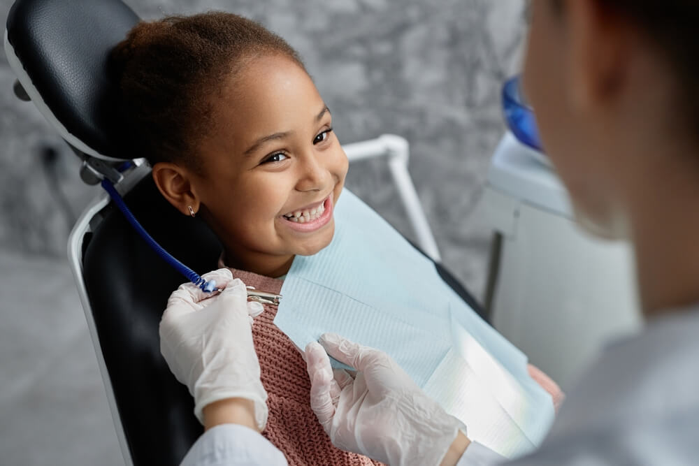 Young girl smiling and showing teeth about to get an exam while looking at dental professional