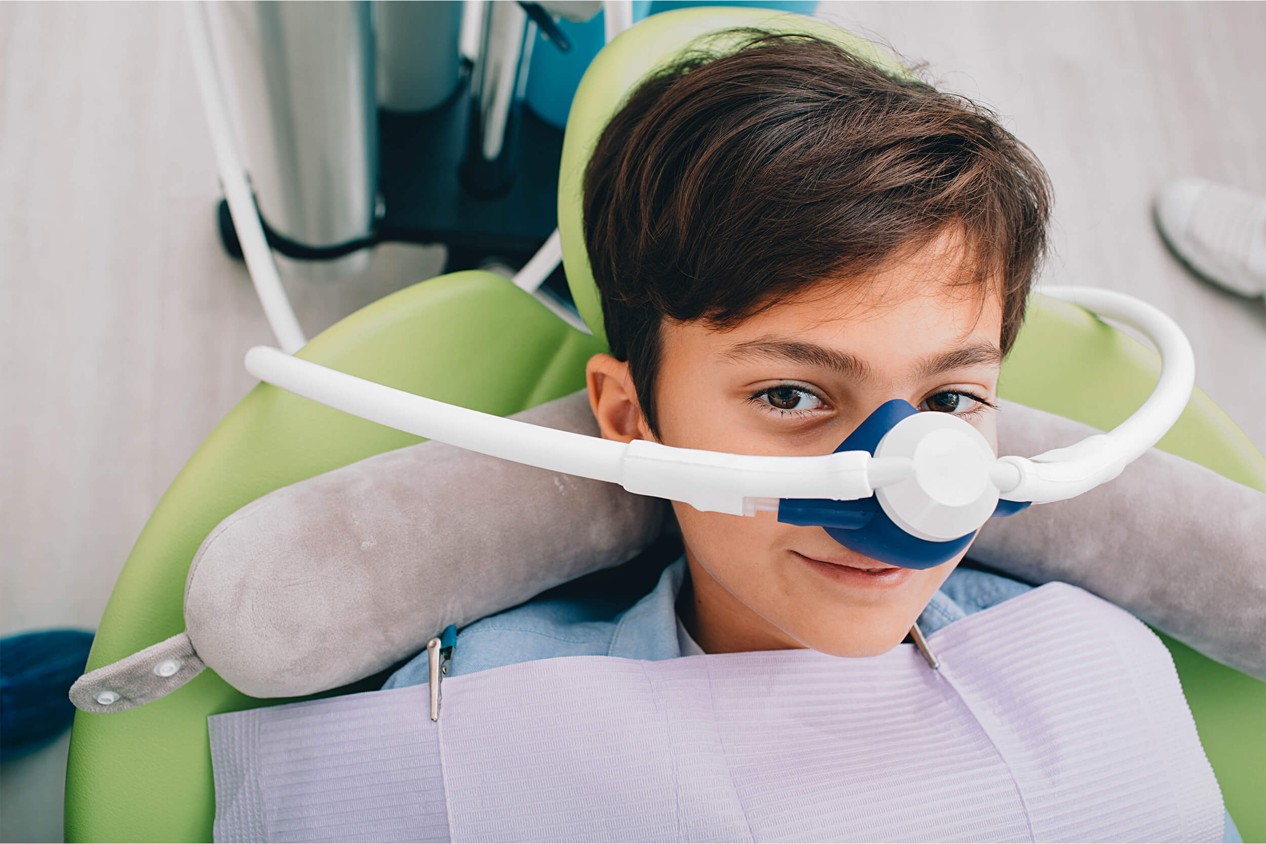 Close up of young boy sitting and smiling in a dental chair with a sedation machine over nose