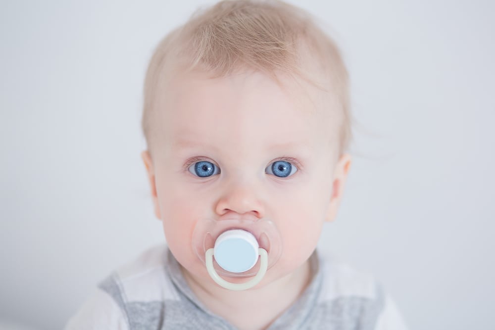 Baby boy using pacifier looking at camera