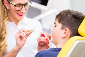 Female dental professional showing model examples of braces to young boy sitting in dental chair