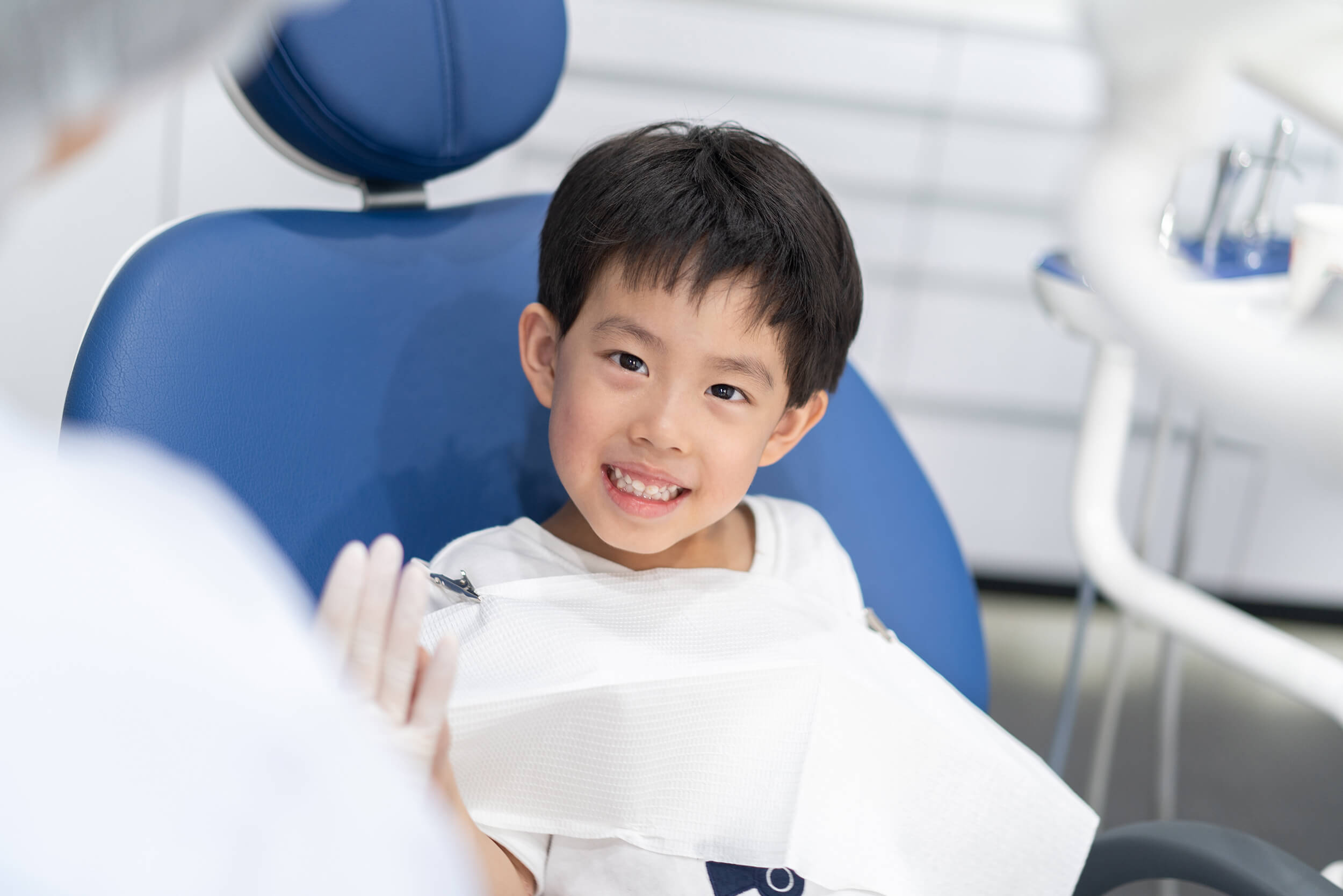 Young boy sitting and smiling with teeth in dental chair while giving the dental assistant a high five