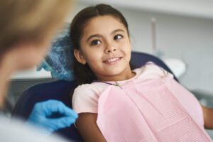 Young girl sitting and smiling with teeth in dental chair looking ad listening at dental assistant