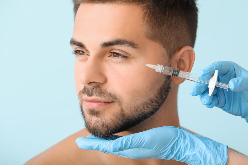 Handsome man receiving filler injection on color background