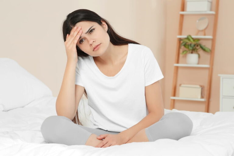Young woman suffering from headache on bed at home. Hormonal disorders