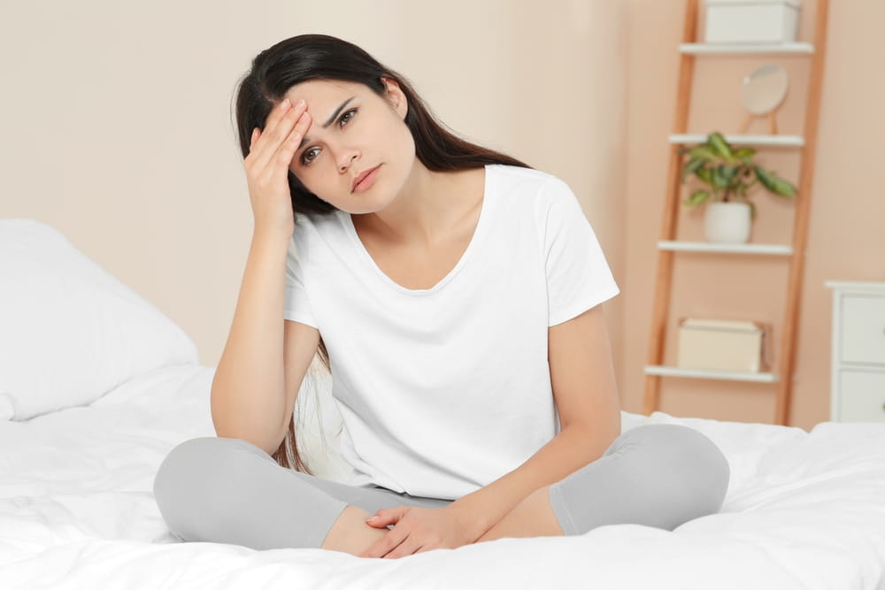 Young woman suffering from headache on bed at home. Hormonal disorders