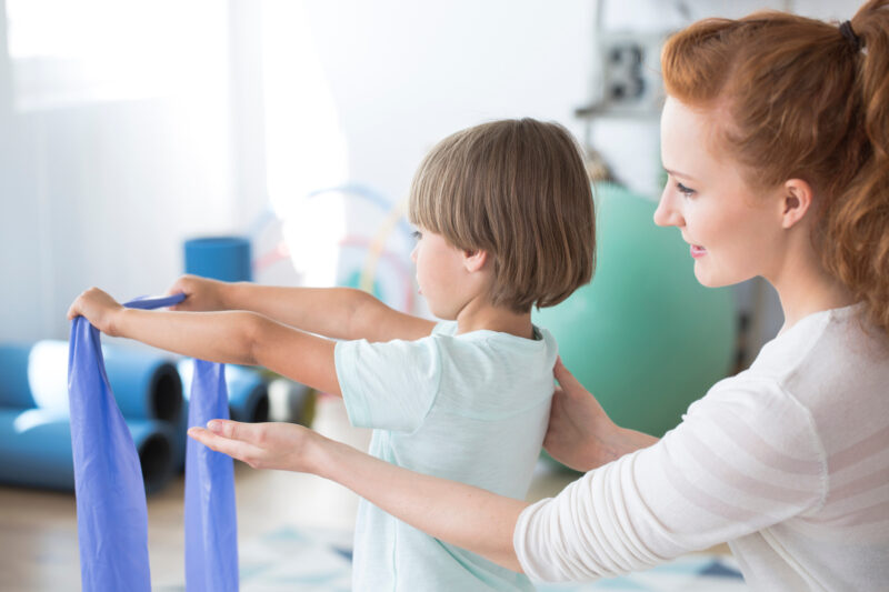 Physiotherapist supporting a kid stretching with violet elastic tape