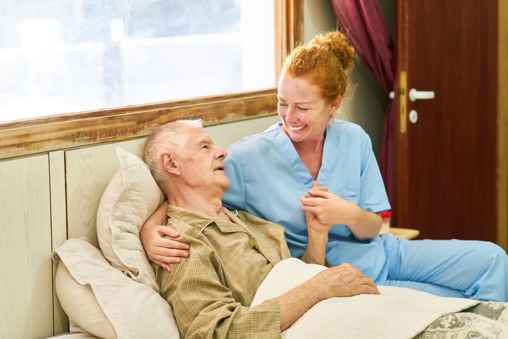 Nurse at the bed of a sick senior holding hands to comfort