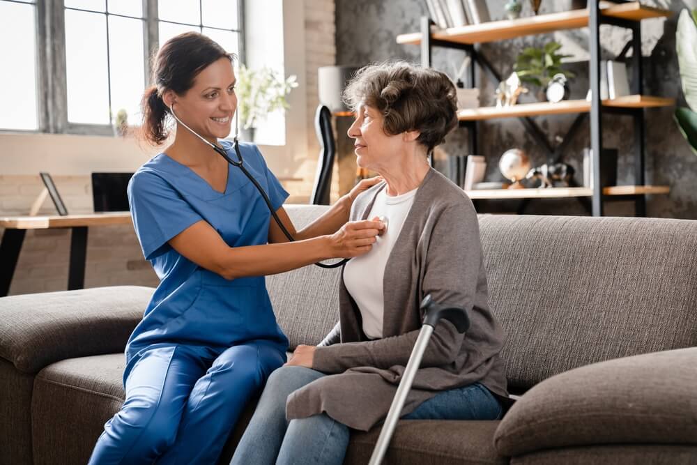 Nurse listening to elderly patient`s heart at home hospice