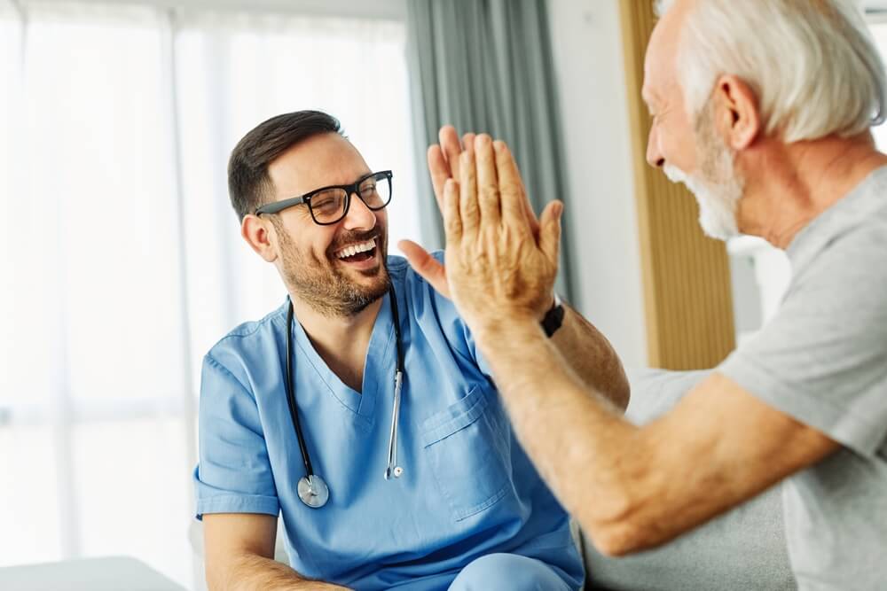 caregiver with senior man giving high five at home